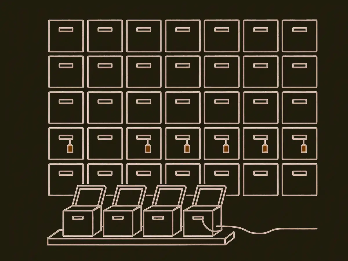 A grid of identical small server crates seen straight on. Roughly a third carry a small tag hanging from one corner. Six crates sit open on a low bench in front of the wall, with a single cable running out of them toward the right.